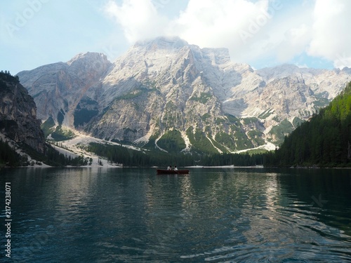 Quadro su tela Scenic view of Lake Braies with tourists in a traditional wooden boat on the calm lake beneath dramatic mountain peaks and forested slopes, Dolomites, Italy