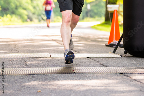 Canvas Print Runner’s legs stride across a road race finish line, passing an orange cone beneath a black inflatable arch, capturing competition, race day and athletic achievement
