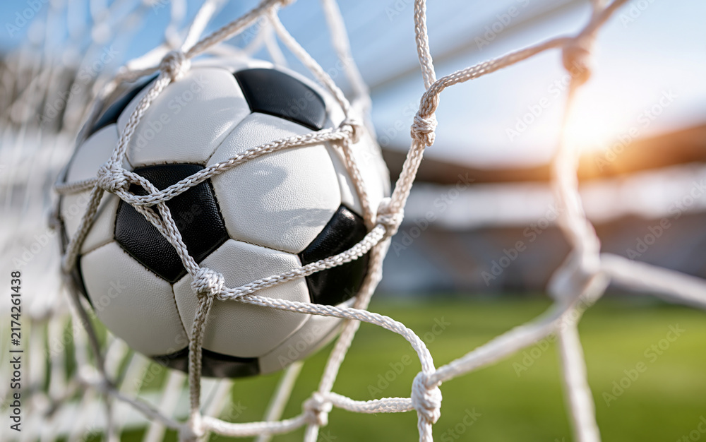 Naklejka premium Soccer ball hitting goal net on green field