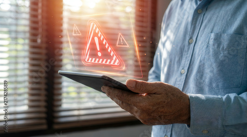 Hand holding tablet with holographic red warning triangle