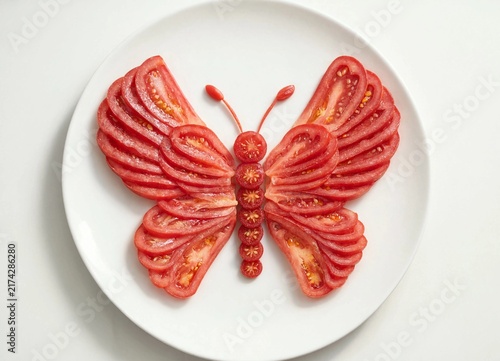 Creative butterfly shaped food art made from sliced fresh red tomatoes on a white plate