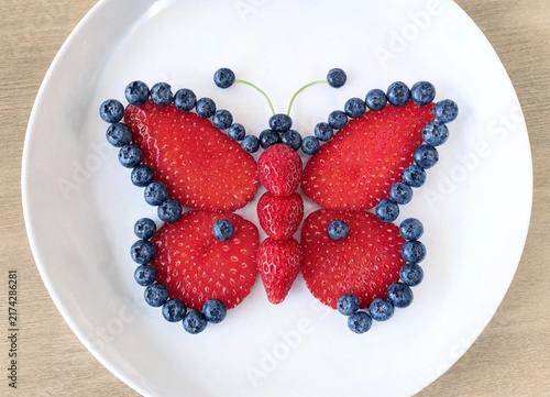 Creative butterfly food art made with fresh strawberries and blueberries on a white plate