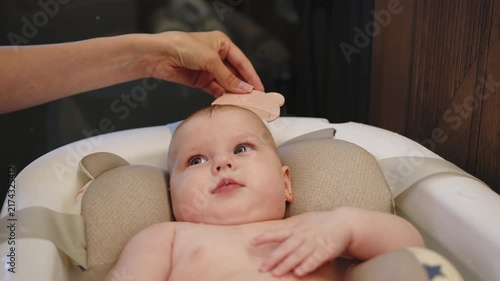 Parent gently combs infants hair during bath time in specialized baby tub with support. A parent gently combs baby hair showing care hygiene and family love