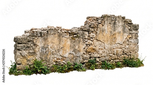 Ancient crumbling stone wall with green plants growing at the base in a rustic landscape