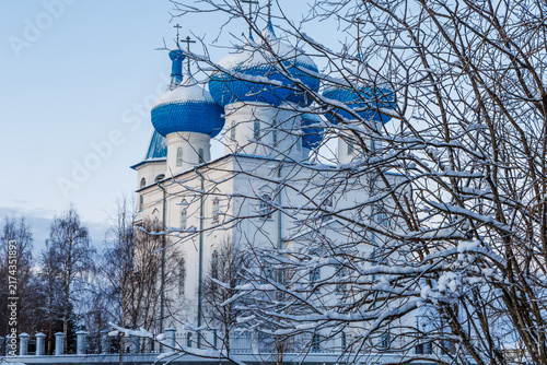 Foto Orthodox stone Sretenskaya Church featuring large bright blue domes behind snowy tree branches in winter Arkhangelsk region, Russia