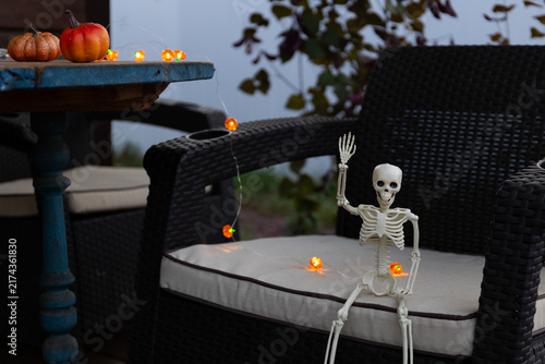 Obraz na plátně Humorous Halloween Skeleton Guest Sits on Veranda, Waving, at Dusk