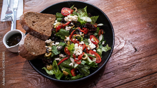 Italian Chopped Salad features vegetables such as tomatoes and lettuce, a sprinkling of Parmesan or provolone cheese, and sliced ​​olives and sourdough bread