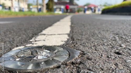 Broken cat eye road reflector embed on asphalt pavement line, low angle shot