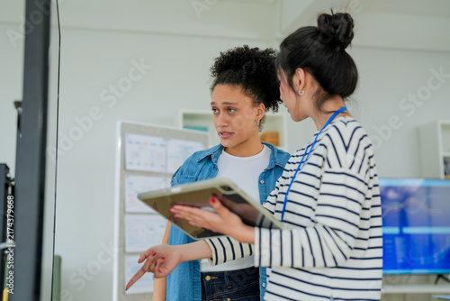 Two colleagues looking closely at a tablet screen, discussing intently from a dramatic low camera angle in a bright office setting.