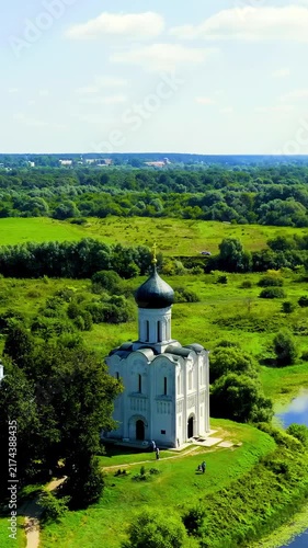 Vertical video. Russia, Bogolyubovo. Church of the Intercession on the Nerl, a white-stone Orthodox church with a single dark dome, Drone footage over the Nerl River floodplain in summer. Drone foota