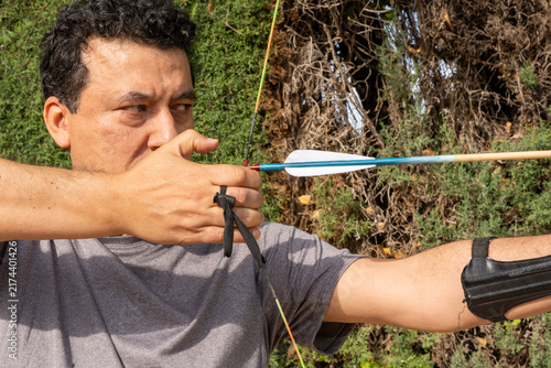 Фотография Man in gray shirt focusing on target during archery training outdoors