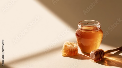 Glass jar of honey with a wooden dipper on a warm neutral surface, natural sweetness, minimalist food, artisanal product.