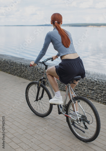 Young sportswoman riding a bicycle along a waterfront promenade. Outdoor cycling, exercise, recreation and active healthy lifestyle in a scenic setting.