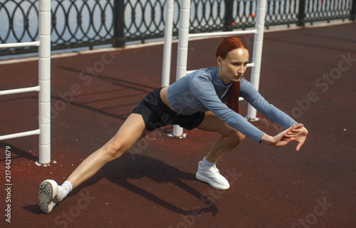 Young woman performing a deep side stretch on a waterfront promenade. Outdoor exercise, flexibility training, warmup and active lifestyle concept.