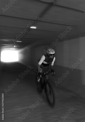 Black and white photo of a cyclist riding through a tunnel road with a blurred background