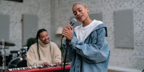 Young female singer rehearsing in a modern music studio with keyboard accompanist for rehearsal background and banner design