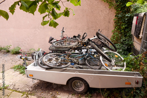 Obraz na plátne Pile of old used bicycles loaded into a small utility car trailer parked outdoors near a wall and green bushes