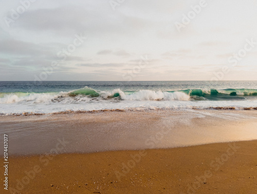 Serene ocean beach with waves breaking near shore with grey sky above