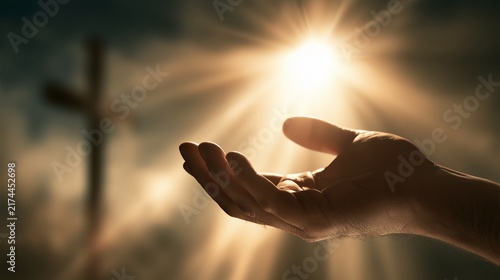 Light shines on a hand reaching out towards the sky with a cross visible in the background during a moment of reflection