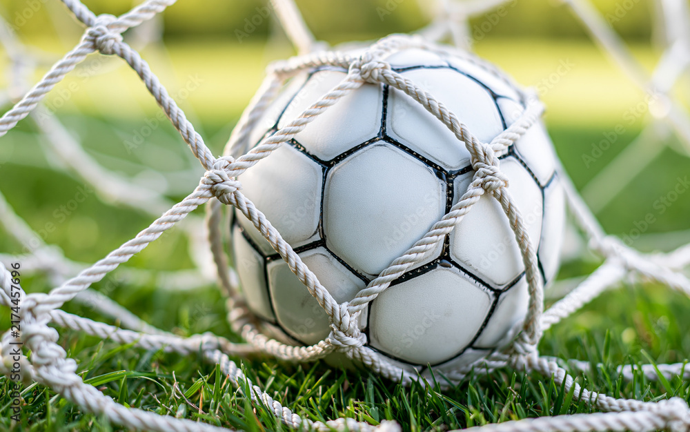 Naklejka premium White soccer ball in goal net on grass field