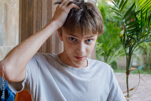 Canvas Print Portrait of a teenage boy with blonde hair sitting outdoors, wearing a gray shir