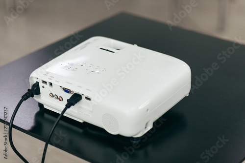White Projector With Connected Cables On Black Desk. Rear View Of Electronic Presentation Equipment Ready For Use.