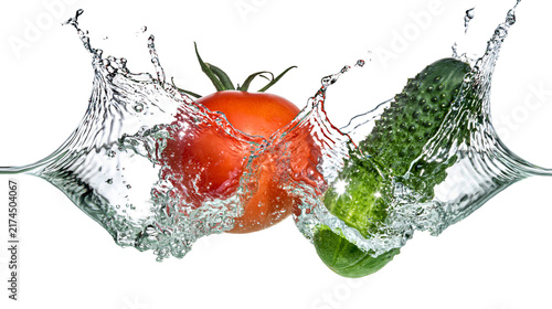 Isolated fresh red tomato and green cucumber splashing into water, creating dynamic clear liquid waves.