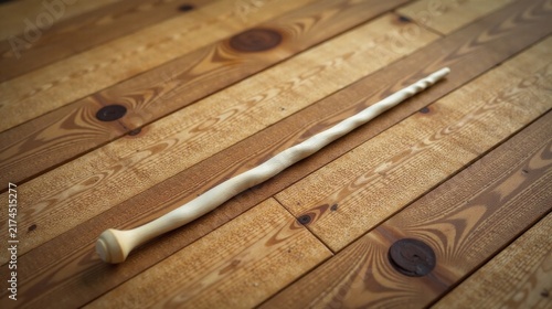 A delicately carved, off-white wand rests on a warm, honey-toned wooden surface, exhibiting intricate craftsmanship.