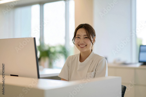 クリニックの受付で笑顔で対応する日本人の医療事務スタッフ

