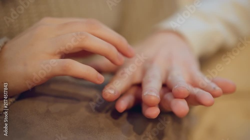 Close up of two hands gently resting and interacting on soft fabric surface with fingers overlapping in calm contact. scene features warm lighting that highlights texture of skin tones