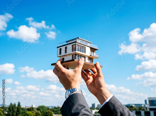 Real estate business concept hands holding house model against clear blue sky property investment