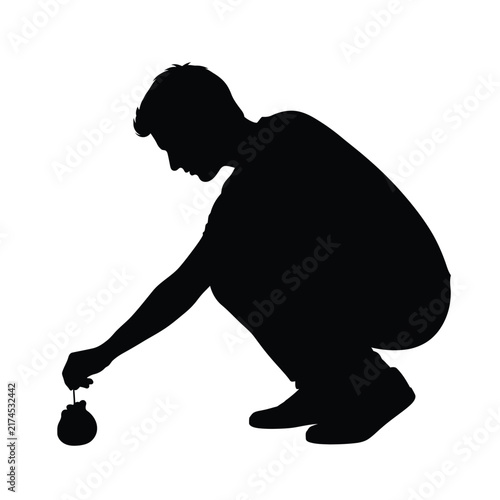 Man kneels down to touch a small object on the ground in silhouette.