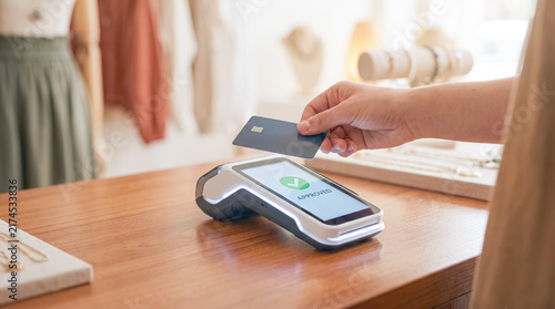 Contactless Payment at the Counter: A hand holds a card to a payment terminal at a store counter, showcasing a modern and convenient way to conduct transactions.