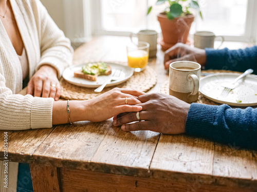 Morning Embrace: A couple's hands intertwined over a rustic wooden table, sharing a tender moment during a breakfast of avocado toast and coffee.
