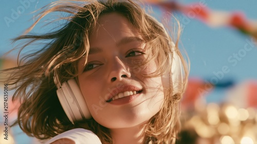 ヘッドホンをつけて風に髪をなびかせる女性のアップ。音楽を楽しむリラックスしたシーンや広告素材