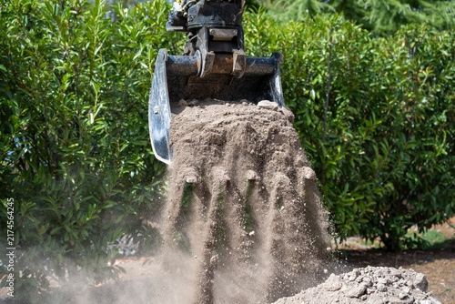 Close-up of an excavator lifting and handling a large root ball during tree removal or transplantation work in a green outdoor environment.