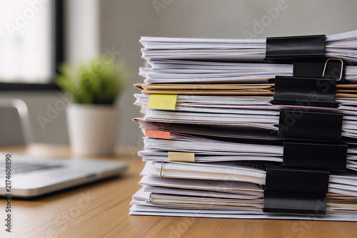 Stack of paper documents and files on office desk with paperwork overload and document management concept
