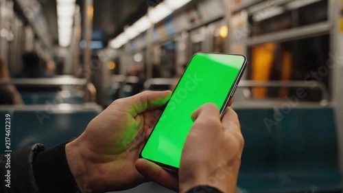 Green Screen Subway Commute, Cinematic close up of hands holding a generic smartphone with a vibrant solid green screen while traveling inside a moving subway train, creating a modern urban technology