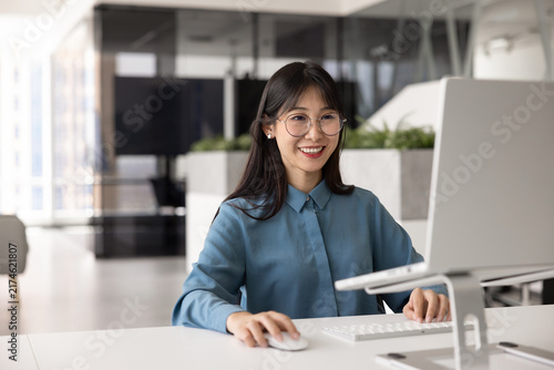 Bild auf Leinwand Smiling Asian woman, staff member working at ergonomically optimized desktop in