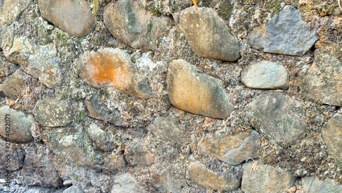 Bild auf Leinwand Old stone wall texture with green moss and weathered river rocks background