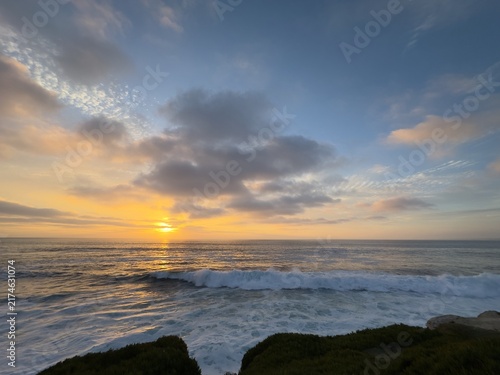 Fotografie Luminous sunset sky with scattered clouds over crashing ocean waves along the coastal shoreline in La Jolla, California