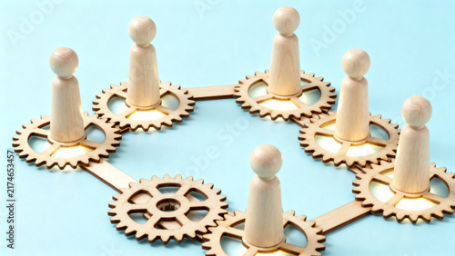 Wooden figures balancing on interlocking golden gears symbolizing teamwork and synergy