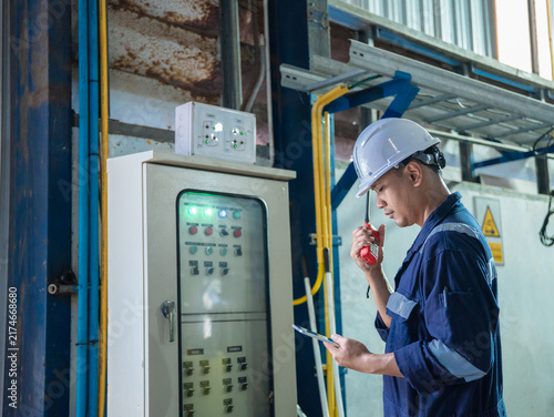 Electrical engineer is communicating with team and use radio while working on digital tablet control electrical panel in industrial plant. System PLC industrial manufacturing. Factory industry 