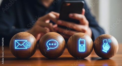Person using smartphone with glowing contact communication icons on wooden balls representing customer service