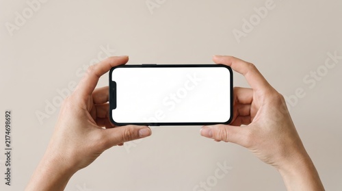 Hands holding black smartphone horizontally with blank white screen mockup isolated on neutral beige, mobile phone display template for app design, user interface presentation