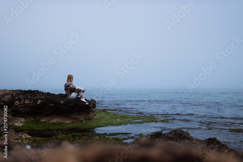 Woman finding peace and tranquility looking out at the foggy calm ocean horizon from a rocky cliff, embracing solitude and mindful reflection
