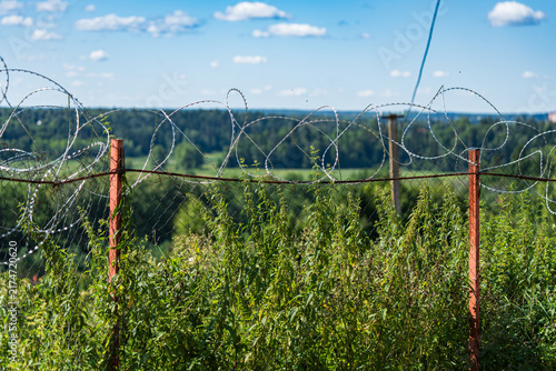 Fotografie Barbed wire fencing atop a rustic fence with a lush landscape in the background
