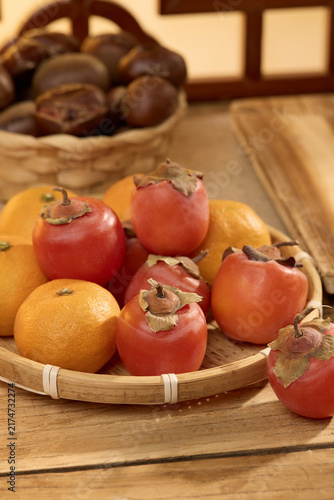 Persimmons and Oranges in a Basket on a Wooden Table