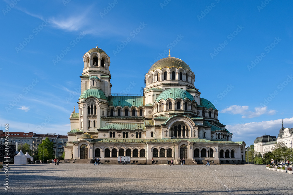 Fototapeta premium Sofia, Bulgaria – Angular exterior view of Alexander Nevsky Cathedral, showing its gold-plated dome and green copper roofs against blue sky.