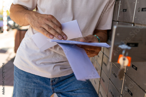 A young man stands at a mailbox with envelopes and reads a letter. Mail recipient. A man stands on the street and holds envelopes in his hands. Close-up of his hands.